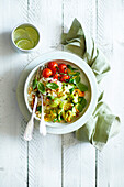 Fried zucchini flowers, fried cherry tomatoes, basil and chopped hazelnuts, served in a white bowl on risotto rice, on a white wooden background