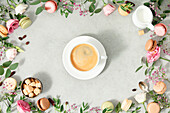 White coffee cup and frame made of spring flowers and different types of macaroons laid flat