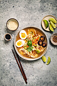 Ramen bowl with noodles, eggs, mushrooms, carrots and sesame seeds on grey background