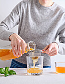 Weibliches Model gießt hausgemachten Bio-Komucha aus einer Flasche in ein Glas und steht dabei auf weißem Hintergrund