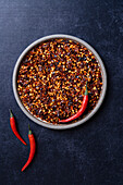 Chilli flakes on a plate of raw chillies on a blue background