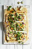 Homemade tarte flambÃ©e with blue cheese, pear chutney, red onions and watercress on a white wooden background