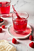 Splash photography of a glass of raspberry hibiscus ginger beer against a light marble background.