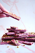 Ruby chocolate made from selected botanical cocoa bean varieties. Dried strawberry and pistachio bark with female hand.