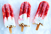 Three homemade strawberry yogurt popsicles on crushed ice