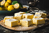 Side angle of square lemon cake slices, topped with powdered sugar, with fresh lemon in background