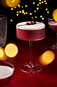 Mulled Wine Sour with Cranberries on Red Surface with fairy lights and glasses