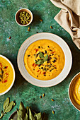 Squash Soup on a Green Surface with Sage and Pumpkin Seeds