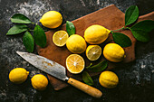 Fresh picked lemons with leaves, some cut in half, on antique cutting board with knife