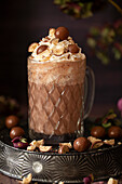 A hot chocolate in a vintage glass mug topped with whipped cream and honeycombe chocolate balls.