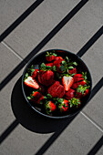 A bowl of strawberries in the blazing summer sun with strong shadows