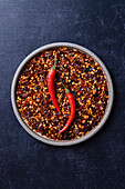 Chilli flakes on a plate with raw chillies on a blue background