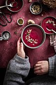 A woman eating beetroot soup with her hands on a red background