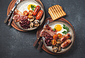 Traditional full English breakfast with fried eggs, sausages, beans, mushrooms, grilled tomatoes, bacon and toasts on gray plates