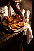 Woman's hands in pink sweater holding a porcelain tray of citrus fruits, on an autumn-winter day.