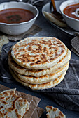 A stack of Turkish bazlama bread on a grey napkin and two bowls of soup behind it.