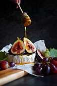 Brie cheese served with figs, honey and grapes. Female hand drizzling honey.