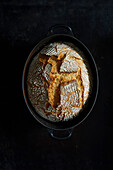 Freshly baked wheat bread in a cast-iron pot on a dark background