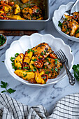 Baked chicken thighs and potatoes served in a white bowl and a fork in it.