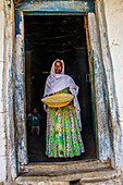 Friendly old woman standing with a basket of corn in a door frame, near Keren, Eritrea, Africa