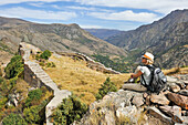 Young woman sitting on a defensive wall of Smbataberd Fortress, on the crest of a hill between the villages of Artabuynk and Yeghegis, near Yeghegnadzor, Vayots Dzor province, Armenia, Eurasia