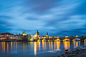 Charles Bridge, OId Town Bridge Tower and dome of St. Francis of Assisi Church by Vltava River at twilight, Prague, Czechia, Europe