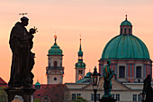 Statue an der Karlsbrücke mit der Kuppel des Heiligen Franz von Assisi im Hintergrund bei Sonnenaufgang, UNESCO-Welterbe, Prag, Tschechische Republik (Tschechien), Europa