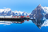 Dusk over the fishing village and the calm water of the fjord surrounded by snowy mountains, Hamnoy, Reine, Moskenes, Lofoten Islands, Norway, Scandinavia, Europe