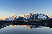 Warmes Morgenlicht auf verschneiten Bergen, die sich in einem Teich am Fjord spiegeln, Vareid, Gemeinde Flakstad, Lofoten, Norwegen, Skandinavien, Europa