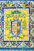 Intricately designed ecclesiastical badge on antique glazed ceramic tiles in the Fine Arts Museum in Seville, Spain.