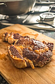 A close-up shot of a grilled steak resting on a wooden cutting board, likely in a kitchen in Seville, Spain. The steak appears to have been cooked to a medium-rare doneness, with a crusty exterior and juicy interior.