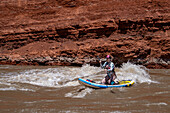 A young woman paddle boarding in the white water of White's Rapid on the Colorado River near Moab, Utah.