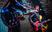 Close up view of a guitarist and singer performing live on stage at a concert with colorful lights shining.