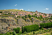 Breiter Panoramablick auf Sepulveda, eine historische Stadt in der Provinz Segovia, Spanien, umgeben von üppigem Grün und dramatischen Hügeln.