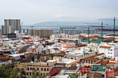 Eine malerische Luftaufnahme der Stadt Gibraltar mit bunten Gebäuden, Kränen und dem Hafen mit angedockten Schiffen.