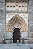 Detailed view of the main facade of the Cathedral of Salvador in Avila, Castilla y Leon, Spain. Visitors entering the historic Gothic architecture.