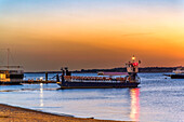 Eine Fähre, die den Fluss Guadalquivir bei Sanlucar de Barrameda bei Sonnenuntergang überquert, mit Blick auf den Donana-Nationalpark, Andalusien, Spanien.