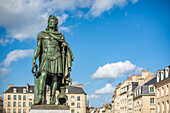 Bronze statue of Louis XIV located in Place Saint Sauveur, Caen, Normandy, France against a backdrop of historical buildings and blue sky.