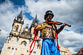 Ein Künstler spielt Geige, während er auf Stelzen bei der Puppenparade vom Marián-Platz zum Altstädter Ring läuft, während des Prager Straßentheaterfestivals Behind the Door, Prag, Tschechische Republik