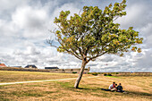 Eine malerische Aussicht auf Menschen, die sich unter einem Baum in der Zitadelle von Port Louis in Lorient, Bretagne, Frankreich, entspannen. Die historische Stätte ist von friedlicher Natur umgeben.