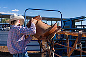 Saddle bronc cowboy Taggyrt Moses picks up his bucking saddle before competing in a rodeo in rural Utah. Note the absence of a saddle horn.