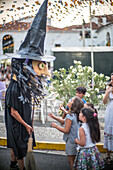 Kinder interagieren mit einer Hexen-Riesenpuppe auf dem Gigantes y Cabezudos-Festival in Fuenteheridos, Huelva, Andalusien, Spanien, das von Familien besucht wird.