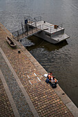 Couple sitting on the edge of the Vltava River, Prague, Czech Republic