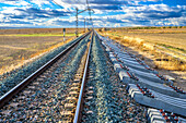 Im Bau befindliche Eisenbahnlinie in Carrión de los Céspedes, Sevilla, Spanien. Klarer blauer Himmel und offene Felder rund um die Gleise.