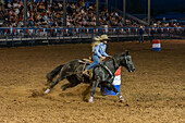 A cowgirl turns around the barrel while competing in the barrel racing event in a rodeo in rural Utah.