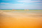 Lang belichtete Aufnahme von Omaha Beach in der Normandie, Frankreich, die das ruhige Wasser und die heitere Atmosphäre des Strandes unter einem klaren blauen Himmel zeigt.