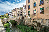 Scenic view of historic buildings and stone bridge over the Darro River in Granada, Spain, showcasing old-world charm and picturesque surroundings.