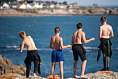 Group of young boys enjoying a sunny day by throwing stones into the sea from a cliff in Ouistreham, Brittany, France.