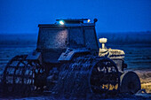 Ein Traktor mit Spezialrädern pflügt nachts ein Reisfeld nach der Ernte in Isla Mayor, Sevilla, Spanien.