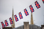 An einer Schnur aufgehängte Union-Jack-Flaggen mit einer verschwommenen Ansicht von Quimper, Bretagne, Frankreich, im Hintergrund.